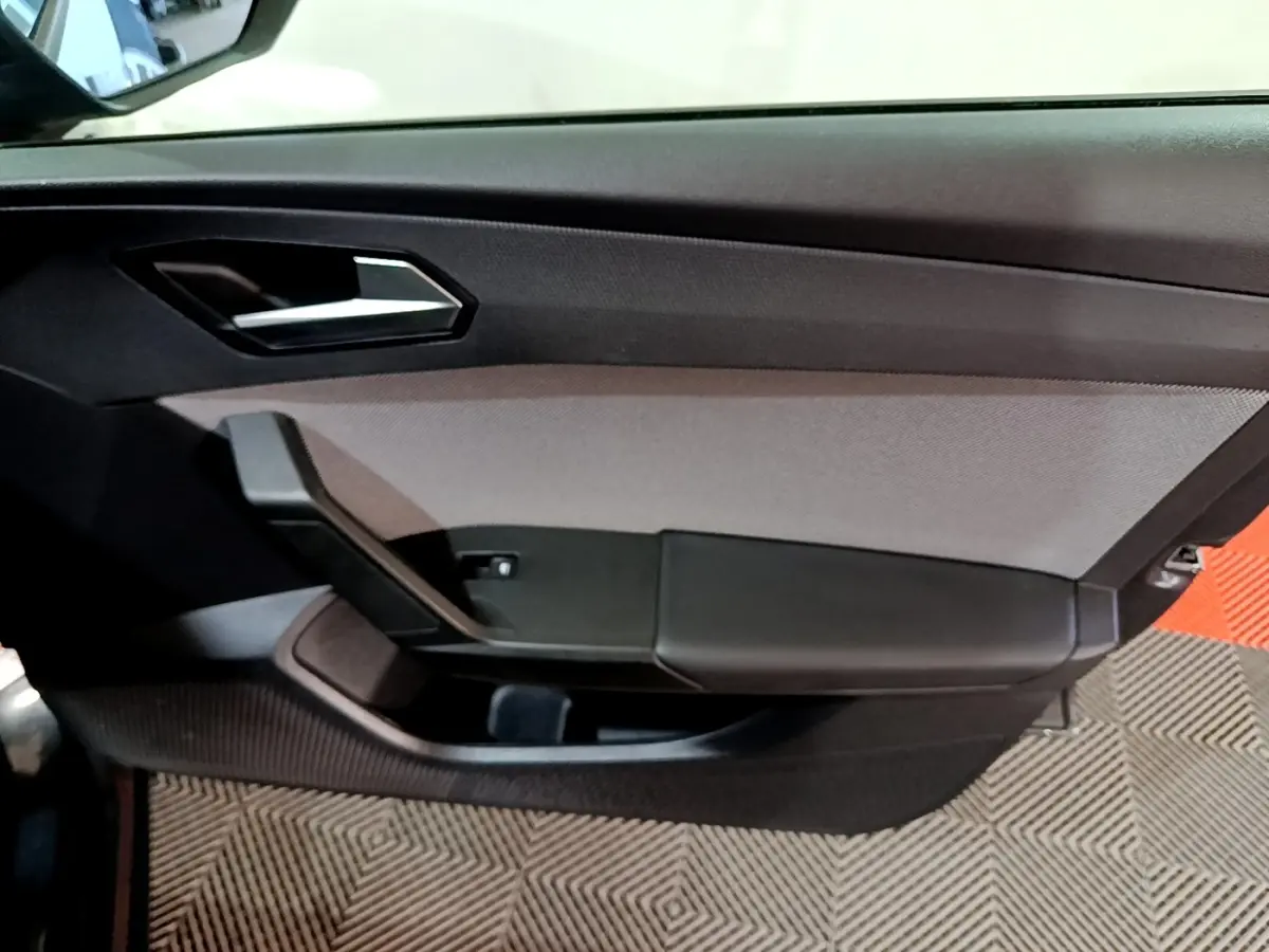 Vue rapprochée de la porte intérieure côté gauche de la SEAT Leon gris clair, avec poignée argentée et panneau noir texturé.