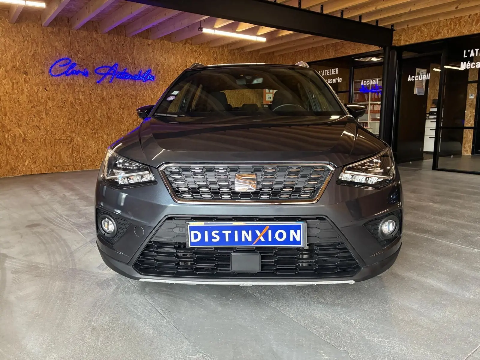 Vue frontale d'un SEAT Arona gris foncé 2021, mettant en valeur sa calandre et ses phares LED dans un showroom.