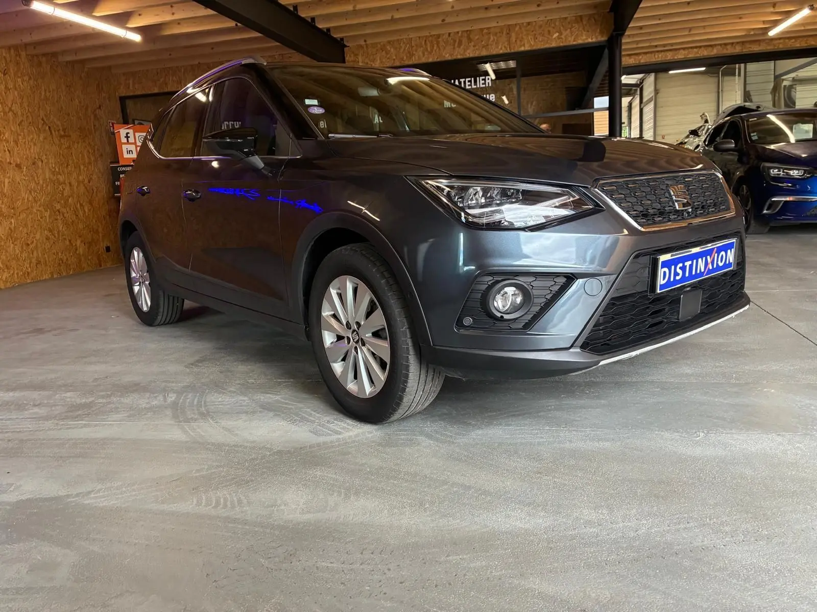SEAT Arona gris foncé vue 3/4 avant droit dans un garage, avec calandre et phares distinctifs visibles.