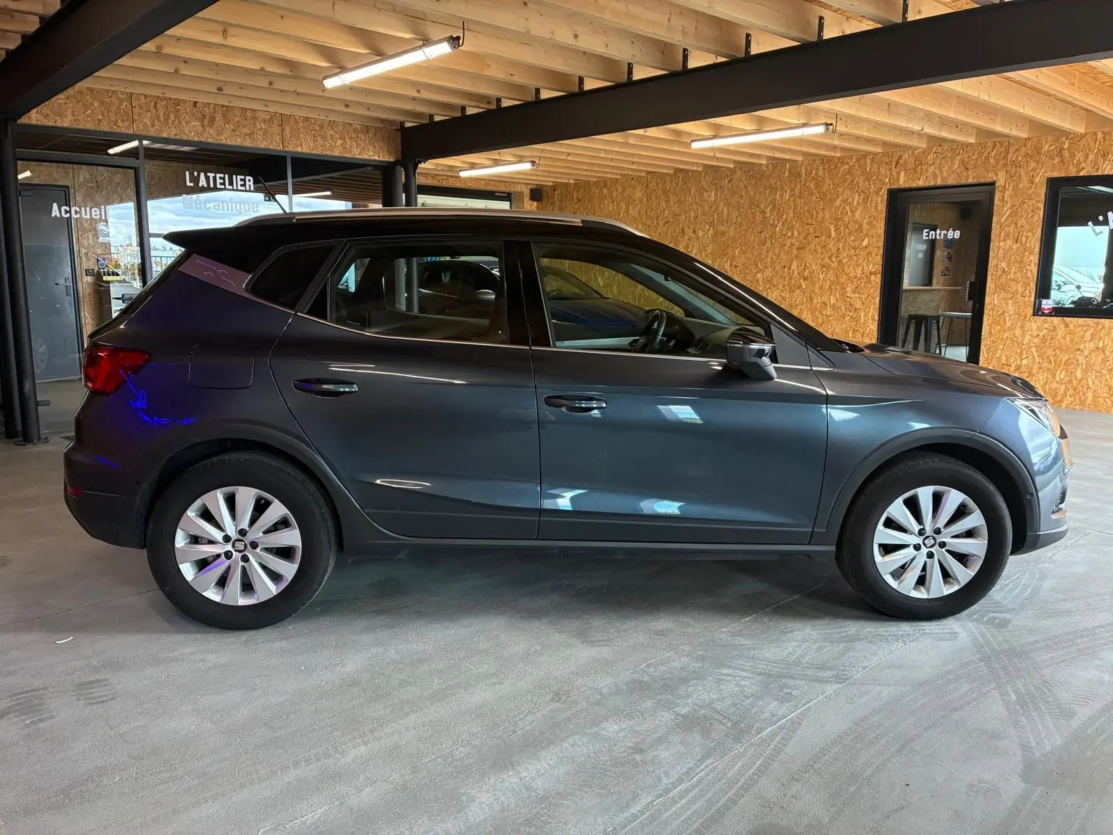 Vue de profil côté gauche d'un SEAT Arona gris foncé 2021 en intérieur, avec jantes argentées et toit noir.