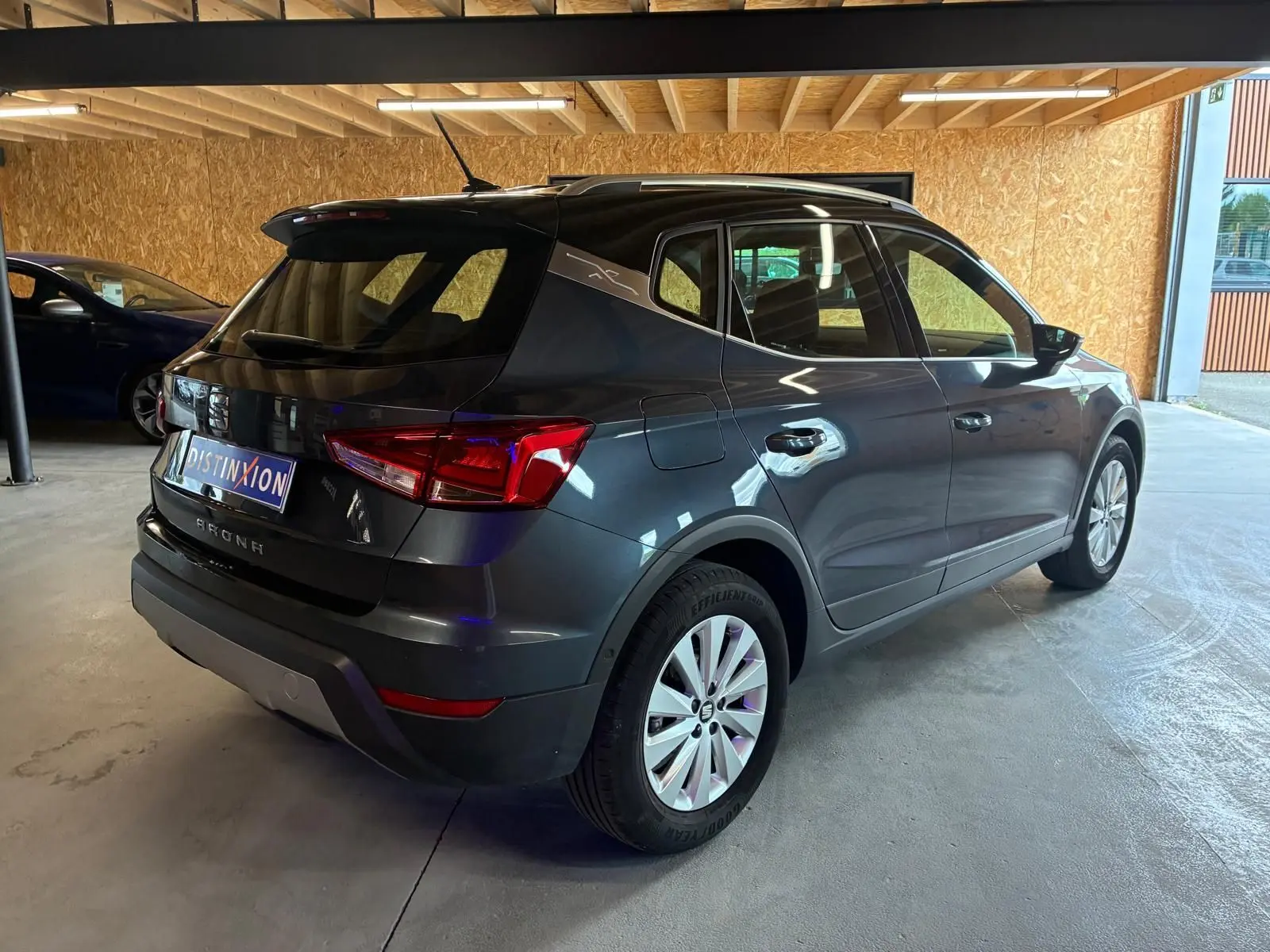 SEAT Arona gris foncé vu en 3/4 arrière droit, avec toit noir et jantes argentées dans un garage.
