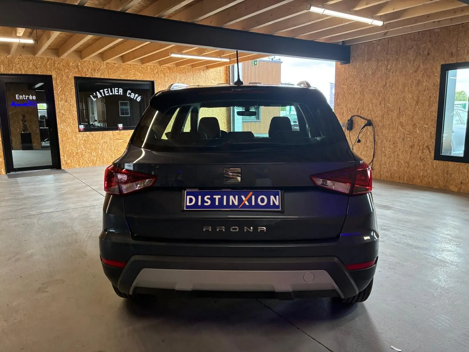 Vue arrière d'un SEAT Arona gris foncé stationné en intérieur avec plaques Distinxion visibles.
