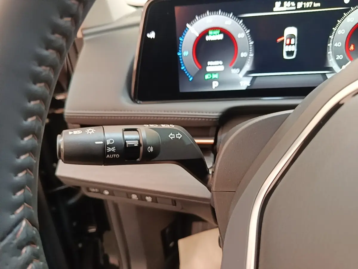 Gros plan sur la manette de clignotants et phares à gauche du volant cuir du Nissan Ariya noir, tableau de bord numérique visible.