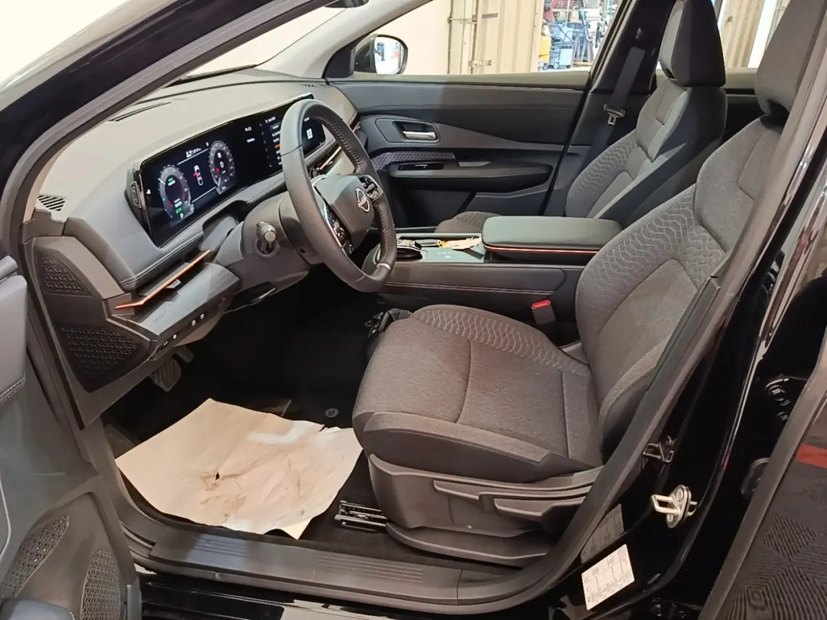 Vue intérieure côté conducteur du Nissan Ariya noir 2026, montrant sièges gris et tableau de bord numérique large.