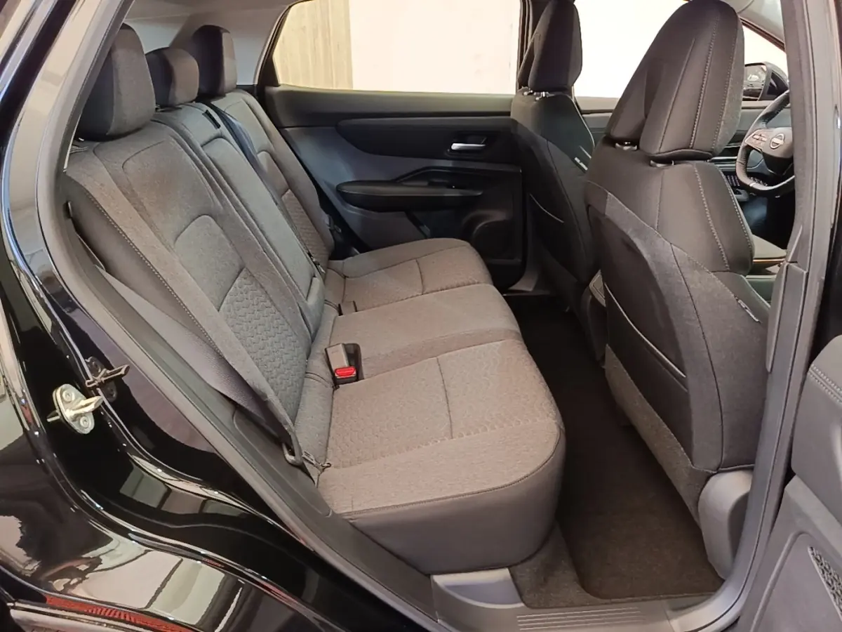 Vue intérieure côté gauche sur la banquette arrière grise du Nissan Ariya noir 2026 avec sièges tissu et ceintures visibles.