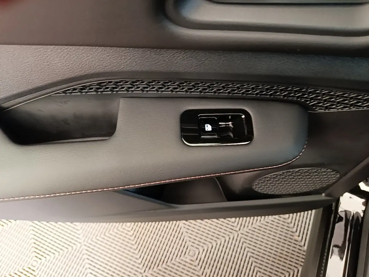 Détail de la porte intérieure côté conducteur du Nissan Ariya noir, montrant la commande de verrouillage et haut-parleur.