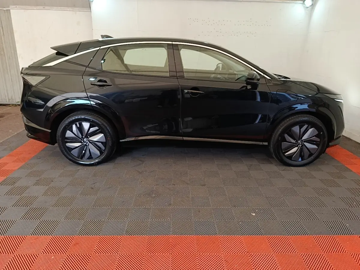 Vue de profil côté gauche du Nissan Ariya noir 63kWh 218ch Engage avec jantes stylisées et toit incliné.