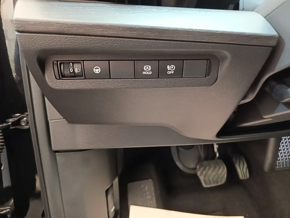 Détail intérieur côté gauche du tableau de bord noir du Nissan Ariya 2026 avec commandes d'assistance et pédales visibles.