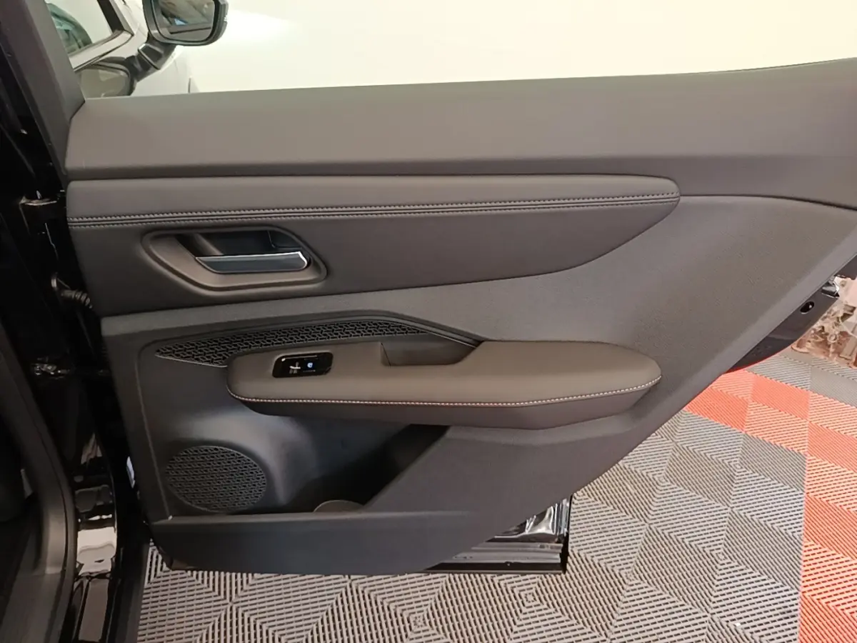Vue intérieure côté gauche de la porte arrière noire du Nissan Ariya 63kWh avec accoudoir et commandes électriques.