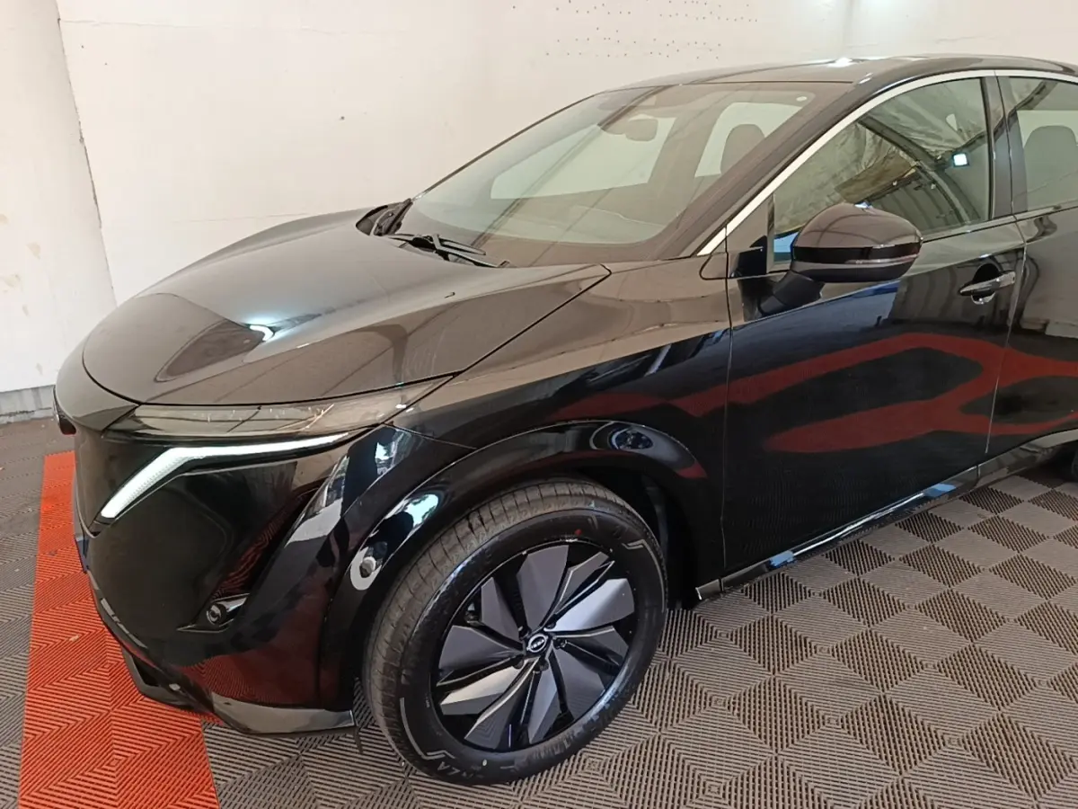 Vue 3/4 avant droit du Nissan Ariya noir 63kWh avec phares LED et jantes design en intérieur fermé.