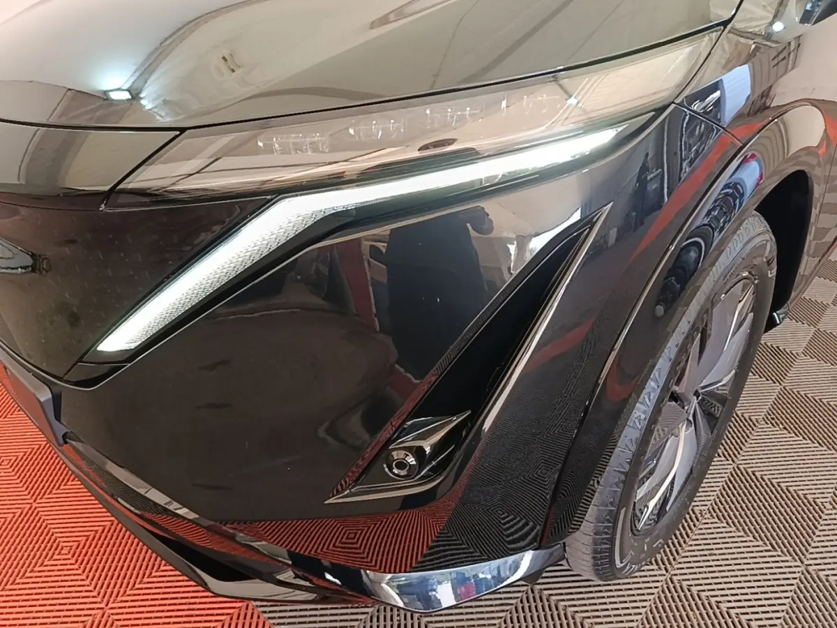 Gros plan sur l'avant droit noir du Nissan Ariya 63kWh 218ch Engage, mettant en valeur le phare LED et la roue.