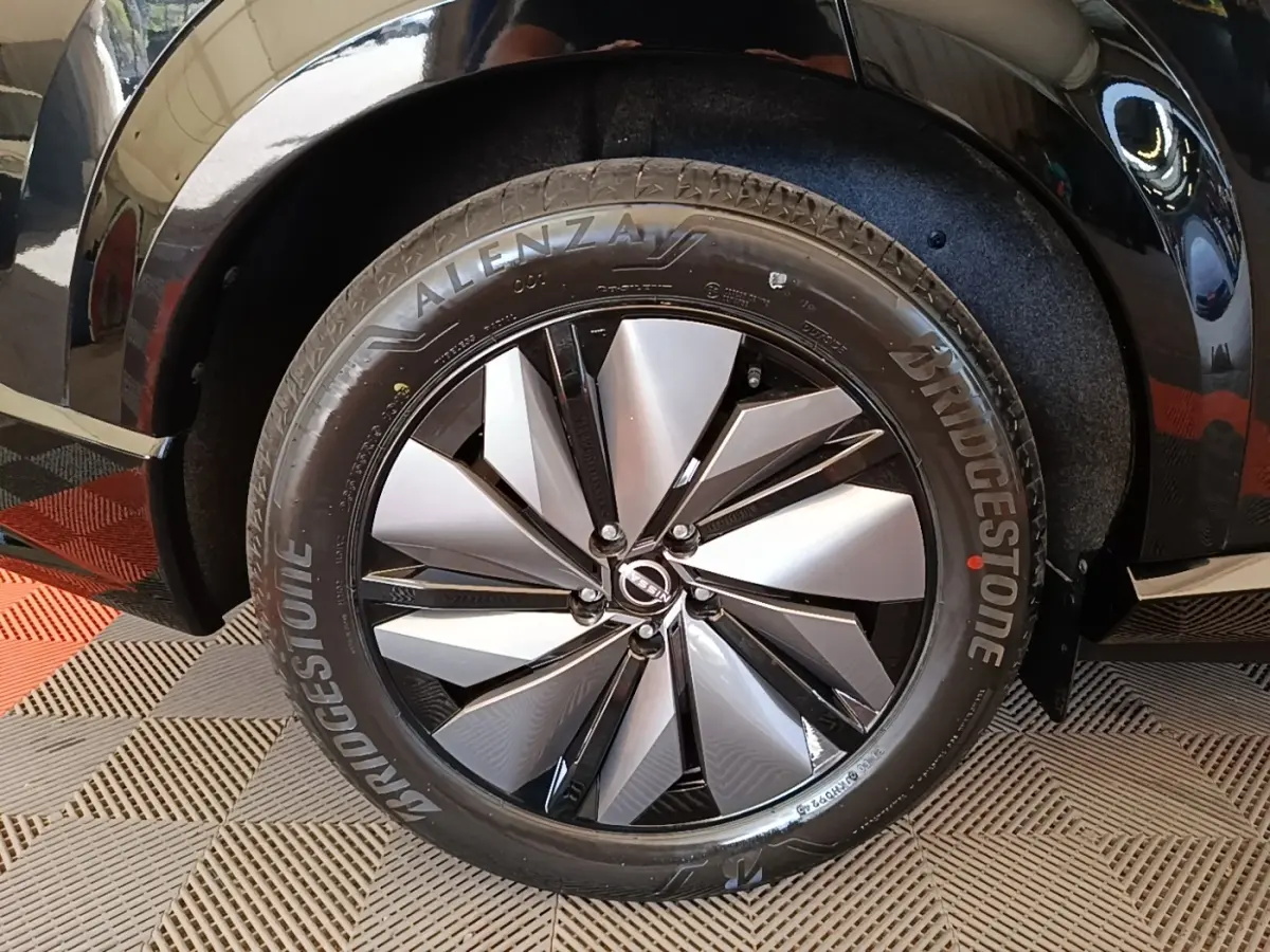 Gros plan sur la roue avant droite du Nissan Ariya noir, mettant en valeur la jante alu bicolore et le pneu Bridgestone.