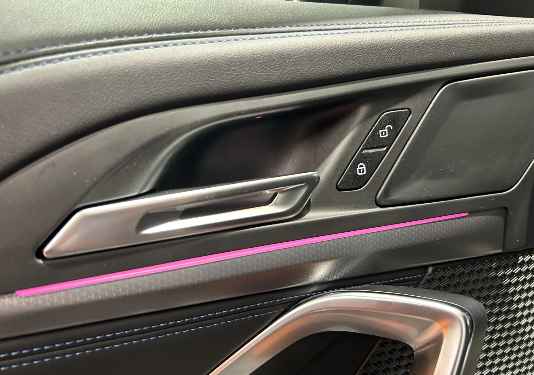 Gros plan sur la poignée intérieure côté gauche du BMW X1 2024 avec éclairage d'ambiance violet et surpiqûres bleues.