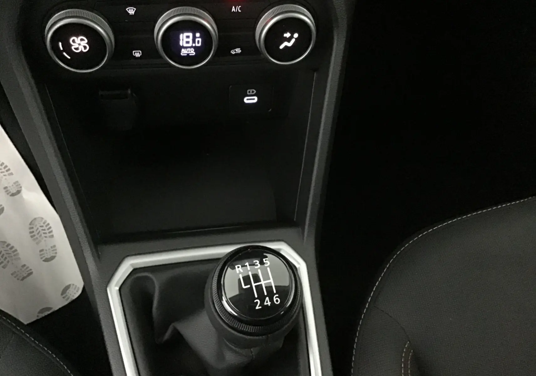 Gros plan sur la commande de boîte manuelle noire et la climatisation digitale à 18°C dans une Dacia Sandero Stepway kaki 2025.