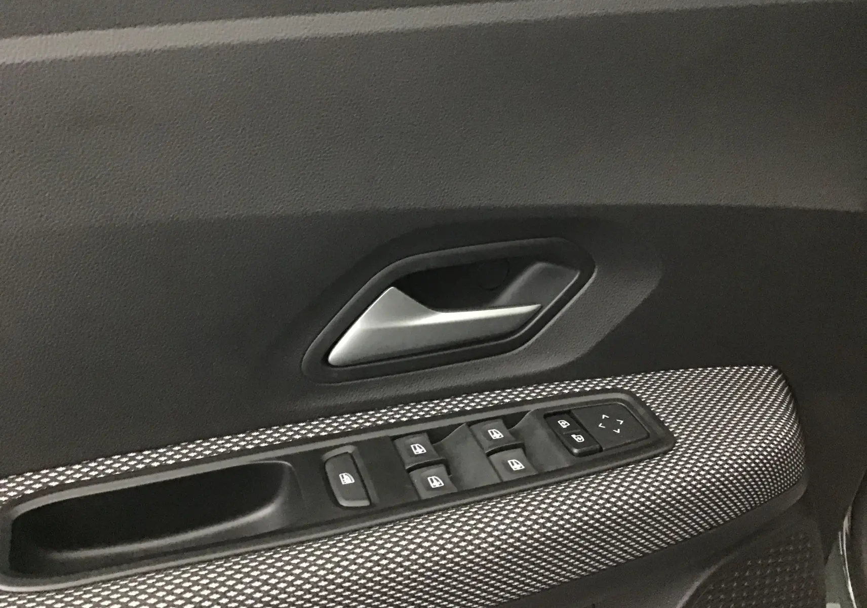 Gros plan sur la commande des vitres et la poignée intérieure côté conducteur de la Dacia Sandero Stepway 2025 en finition Expression.