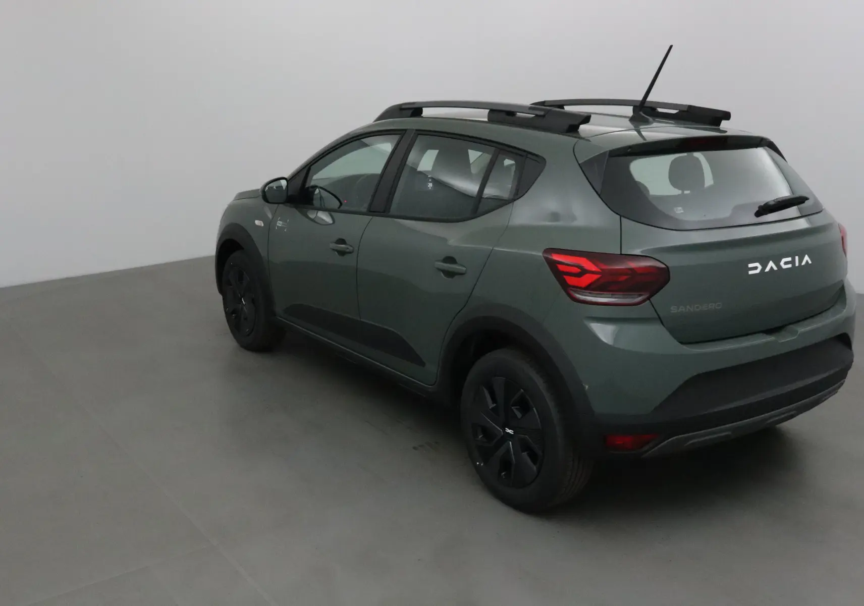 Vue 3/4 arrière droite d'une Dacia Sandero Stepway 2025 kaki avec barres de toit et jantes noires.
