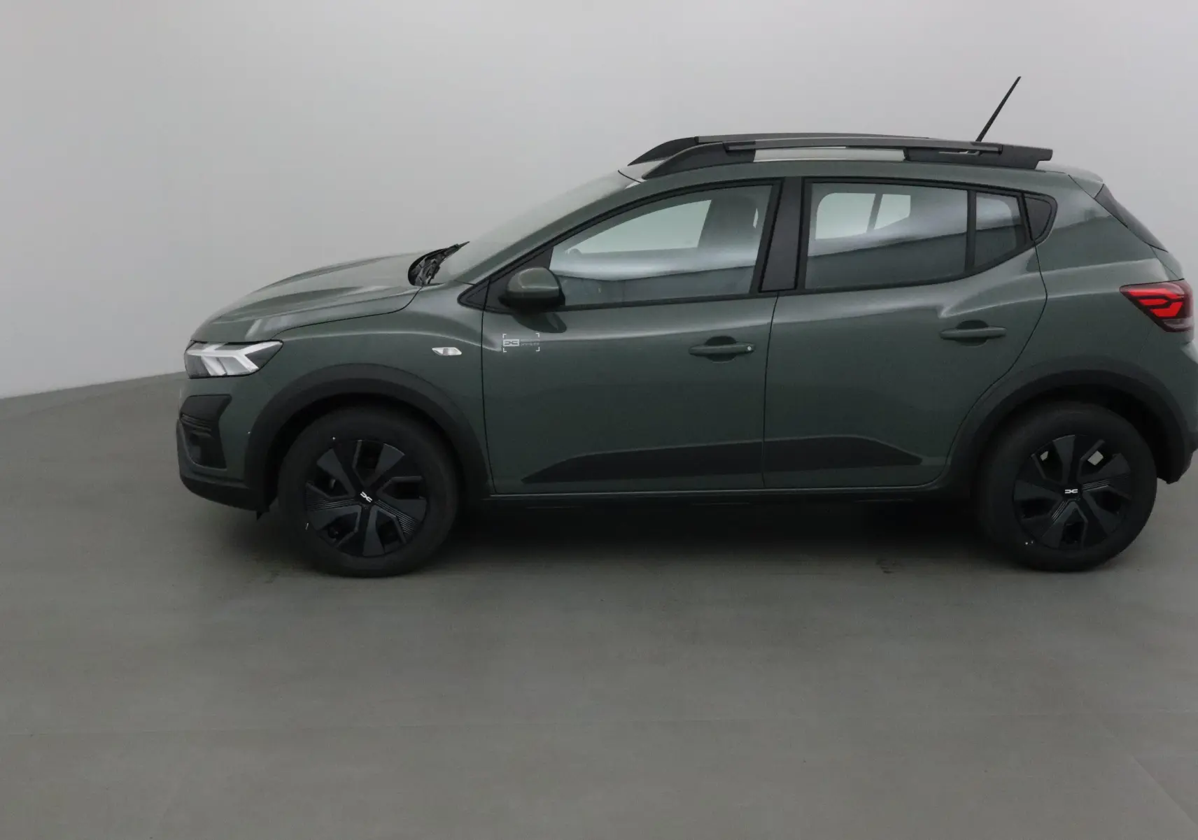 Profil côté gauche d'une Dacia Sandero Stepway 2025 en kaki avec jantes noires et barres de toit noires.