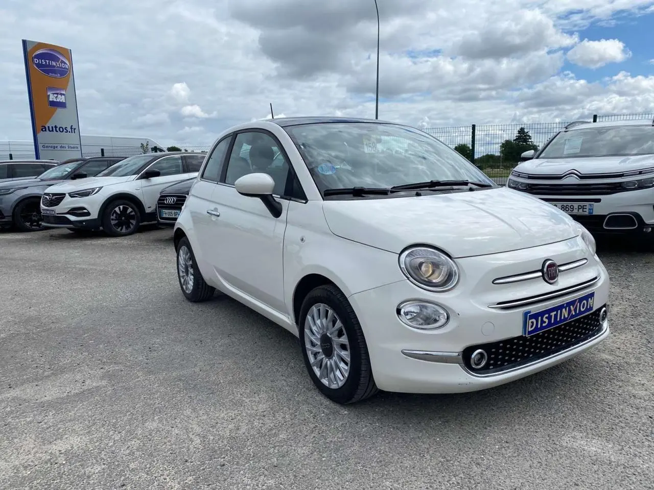 Vue 3/4 avant d'une Fiat 500 blanche avec jantes alliage 16'' Spider et toit panoramique visible.