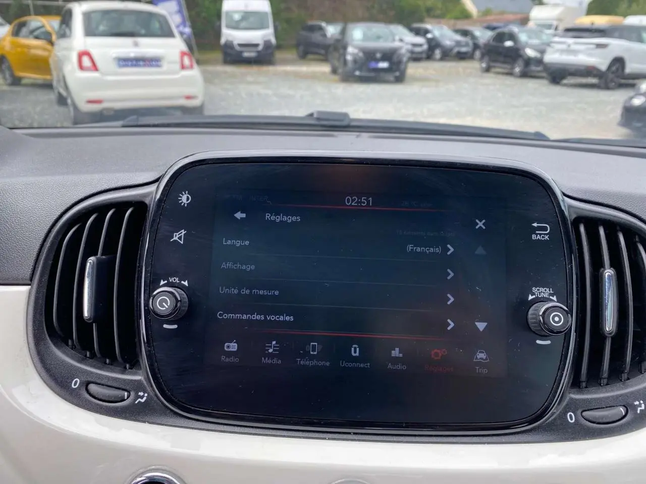 Écran tactile central du tableau de bord d'une Fiat 500 blanche, avec commandes et aérateurs latéraux visibles.