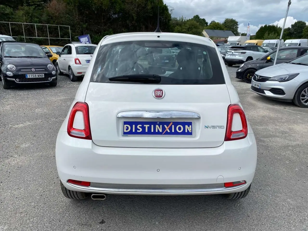Vue arrière d'une Fiat 500 blanche 2024 avec badge Hybrid et radar de recul sur un parking extérieur.