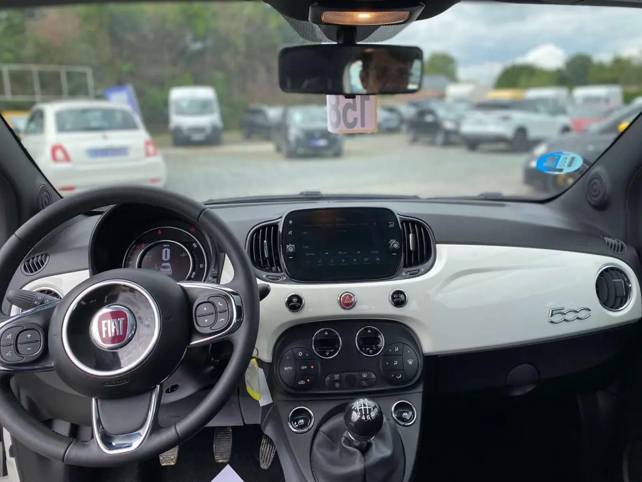 Vue intérieure avant du tableau de bord blanc et noir d'une Fiat 500 2024 avec volant multifonction et boîte manuelle.