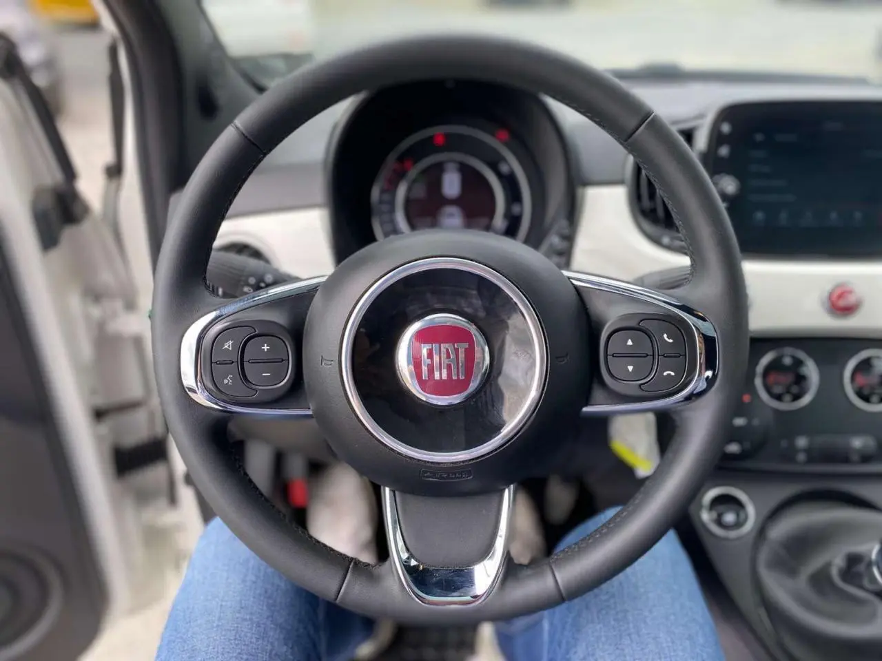 Vue rapprochée du volant noir de la Fiat 500 blanche 2024 avec commandes intégrées et tableau de bord visible.