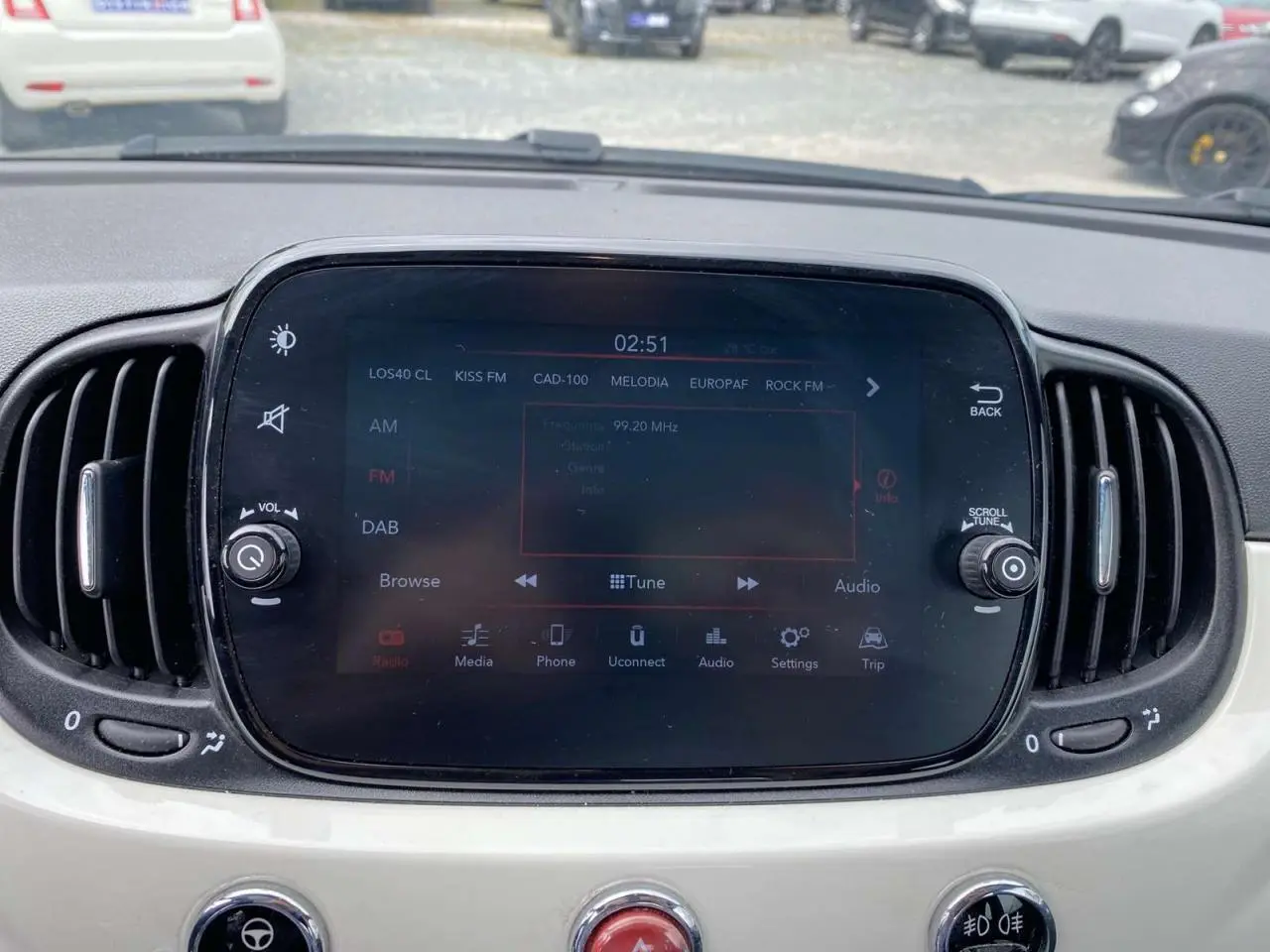 Vue rapprochée de l’écran tactile central du tableau de bord blanc d’une Fiat 500 2024 avec commandes audio et climatisation.