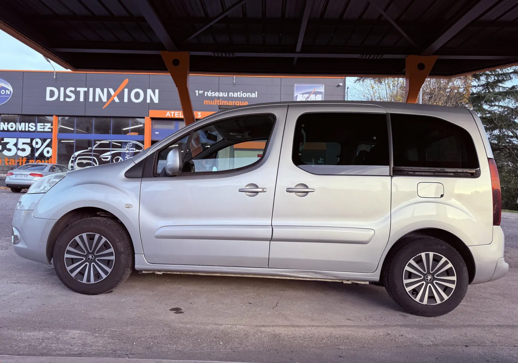 Profil côté gauche d'un Peugeot Partner Tepee gris 2014, montrant ses portes coulissantes et ses jantes distinctives.