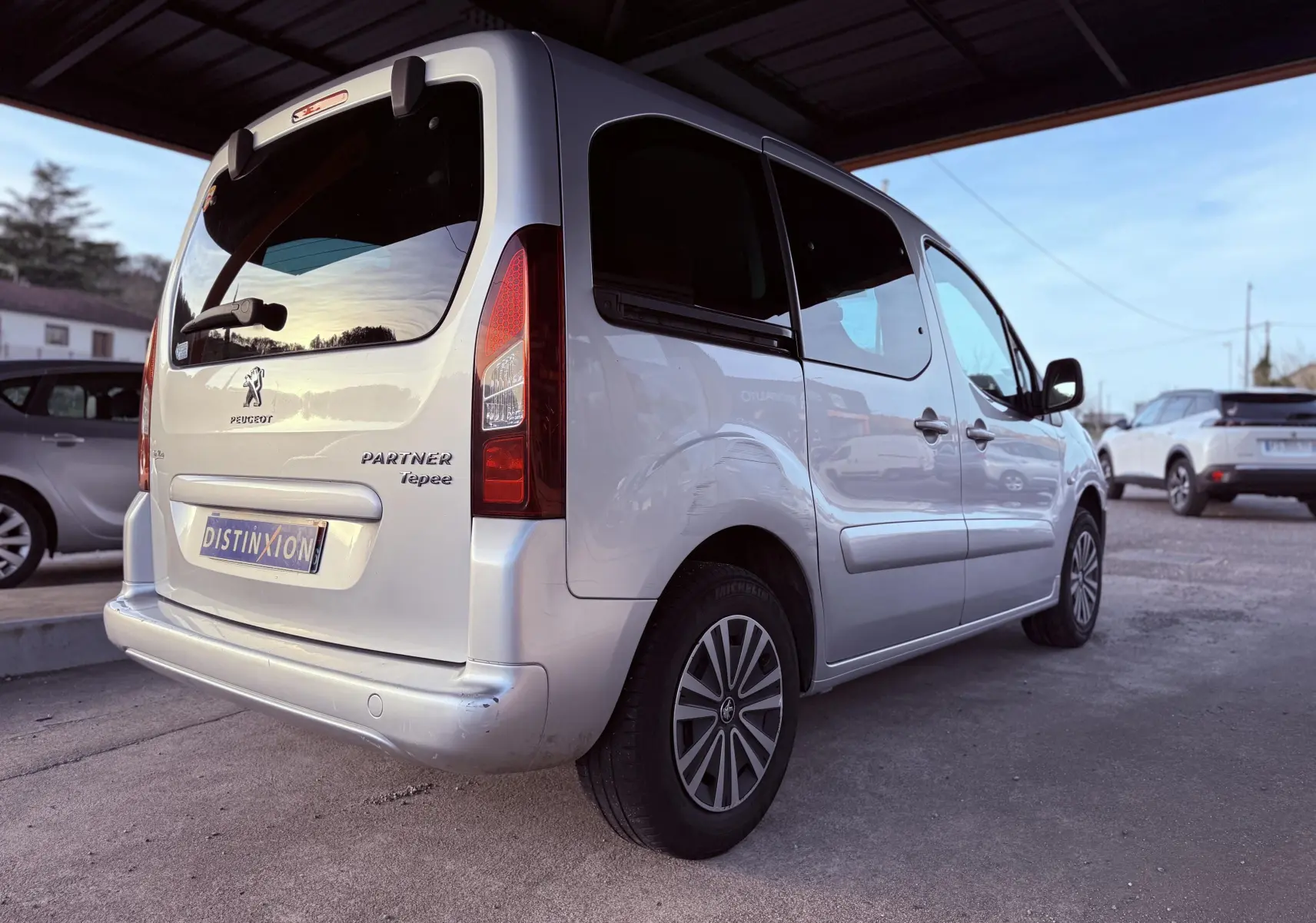 Vue 3/4 arrière droite d'un Peugeot Partner Tepee gris 2014 avec vitres teintées et jantes alliage.