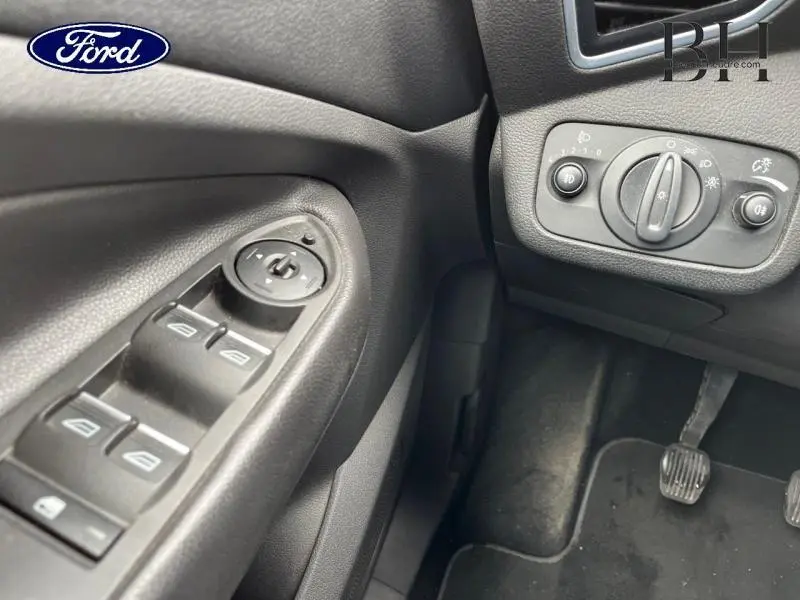 Détail intérieur côté gauche montrant les commandes des vitres électriques et le tableau de bord noir du Ford Kuga gris Magnetic.