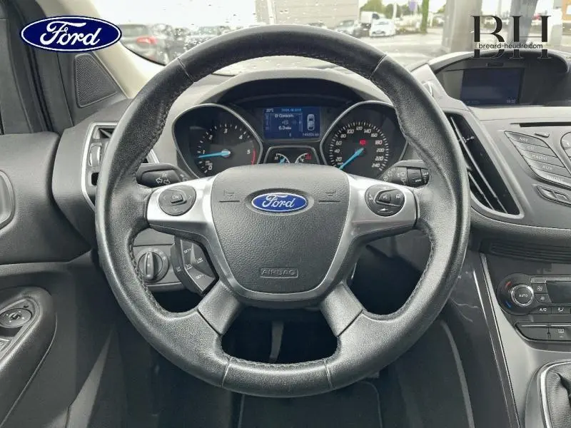 Vue intérieure centrée sur le volant cuir multifonction du Ford Kuga gris Magnetic, avec tableau de bord et écran multifonction visible.