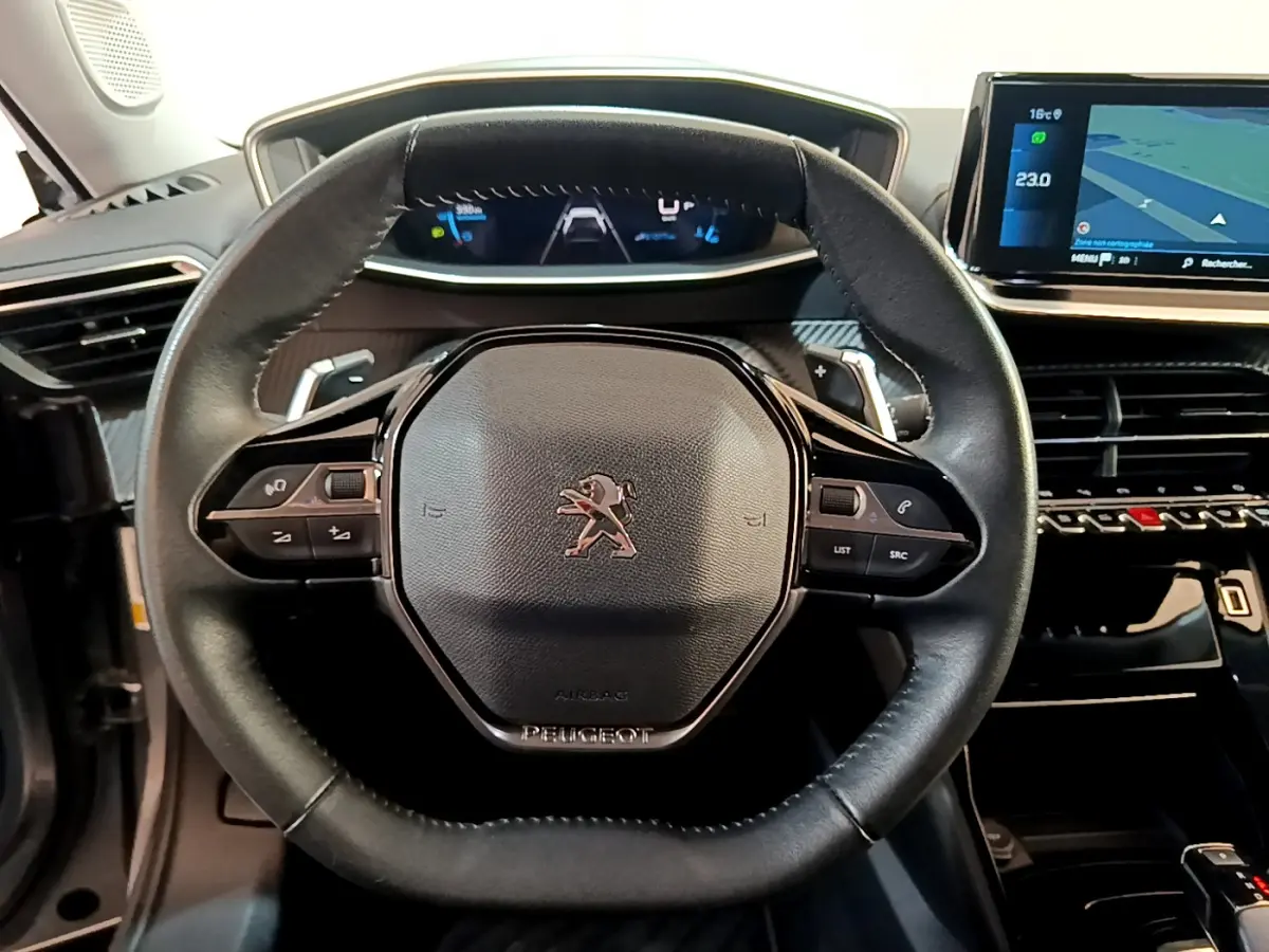 Vue rapprochée du volant cuir multifonctions de la Peugeot 2008 gris clair avec tableau de bord numérique et écran tactile.