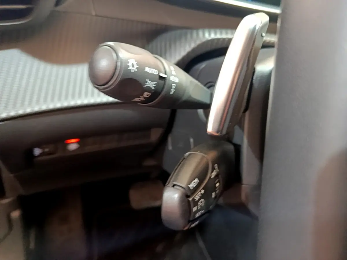 Gros plan sur les commandes au volant du Peugeot 2008 gris clair, mettant en valeur les leviers multifonctions et le tableau de bord.