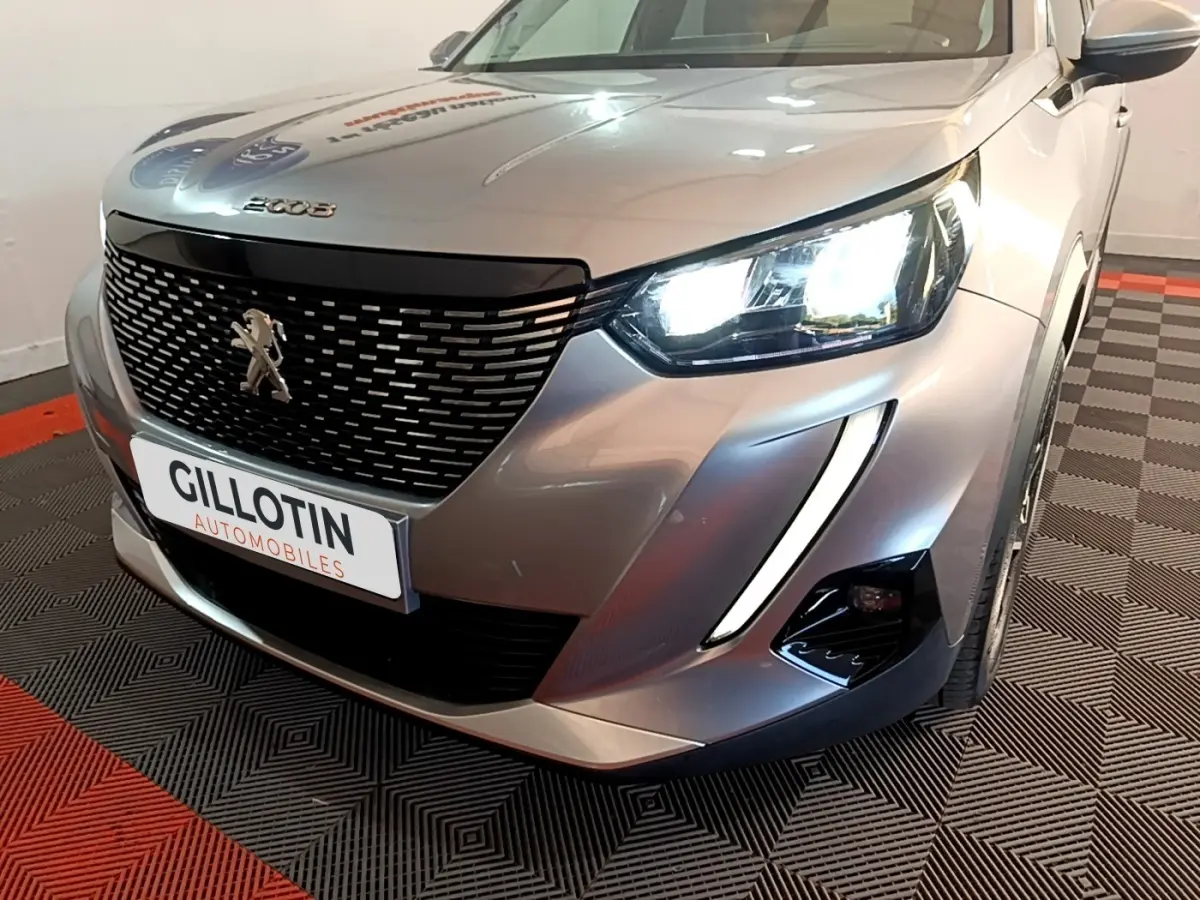 Vue 3/4 avant droit d'un Peugeot 2008 gris clair avec phares LED allumés et calandre noire distinctive.
