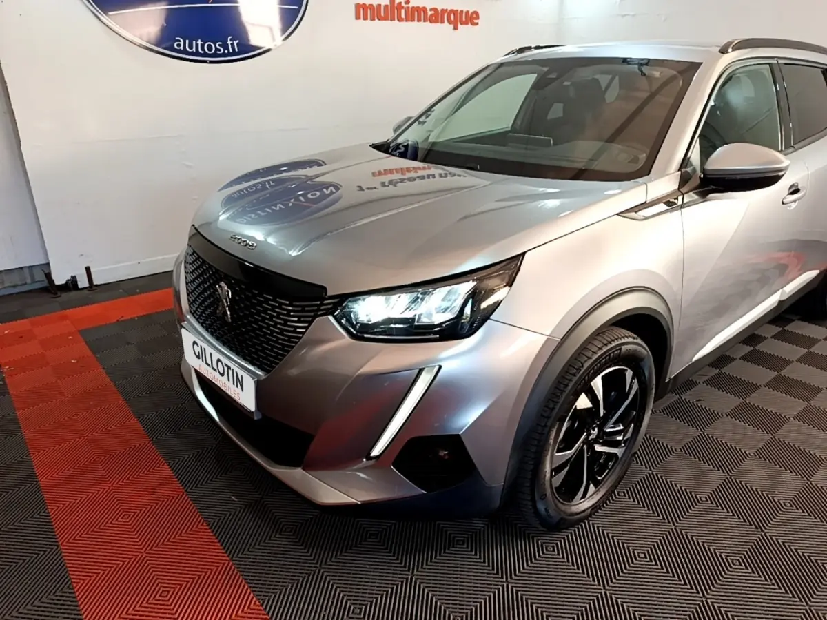 Peugeot 2008 gris clair en 3/4 avant droit, phares LED allumés et jantes noires distinctives.