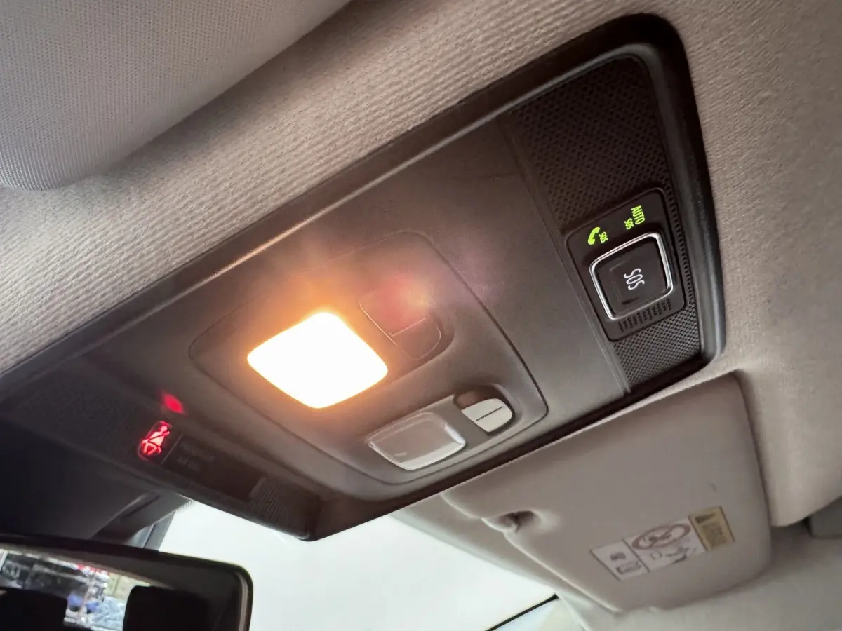 Plafonnier intérieur allumé avec bouton SOS et éclairage d'ambiance dans une Renault Clio blanc, vue en léger contre-plongée.