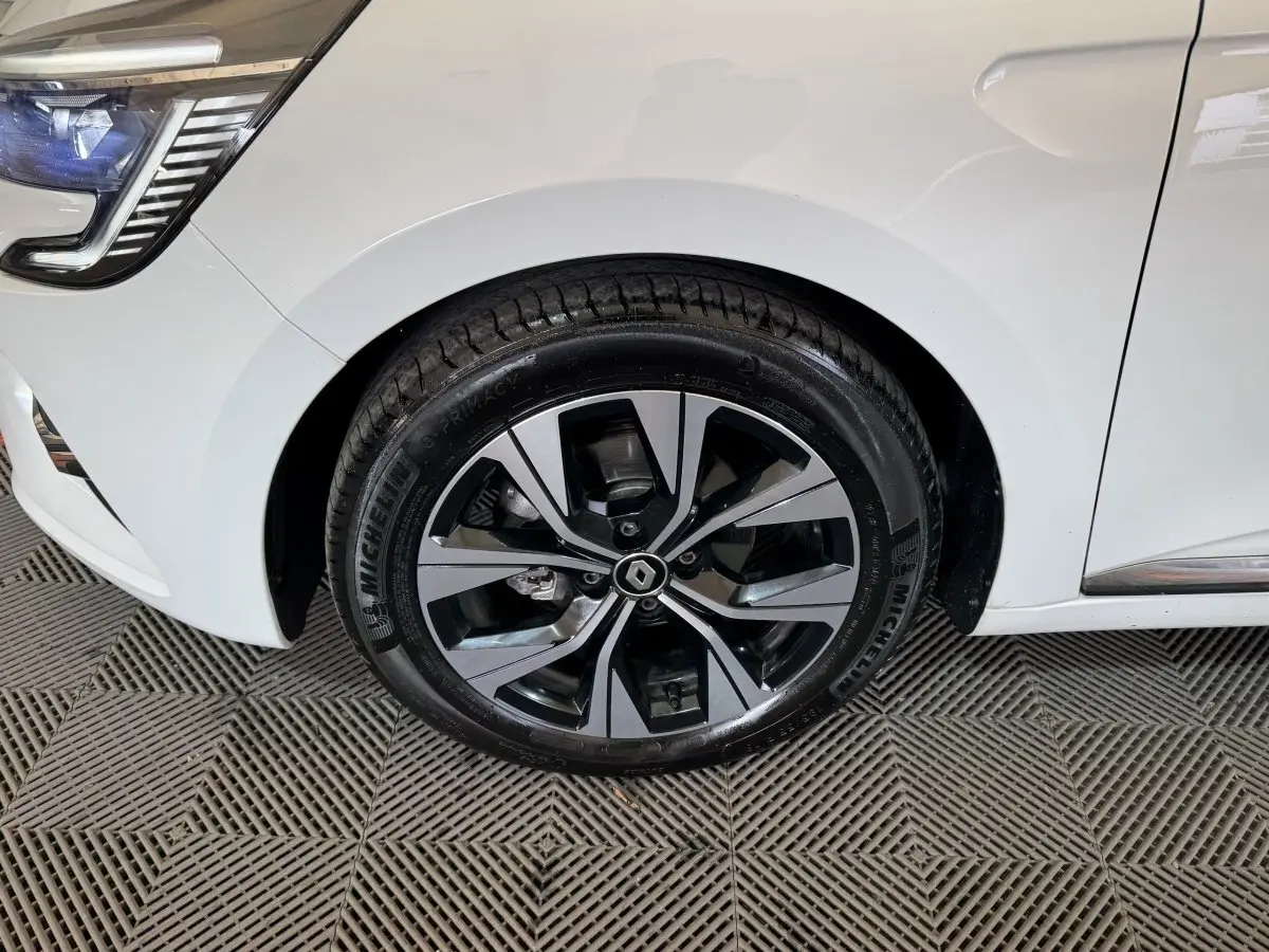 Gros plan sur la roue avant gauche de la Renault Clio blanche avec jante alliage au design moderne et logo Renault central.