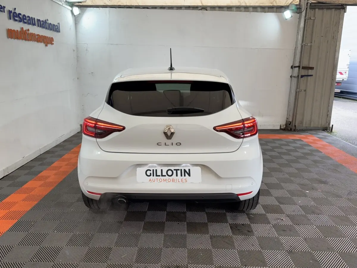 Vue arrière d'une Renault Clio blanche 2023 avec feux LED allumés dans un garage.