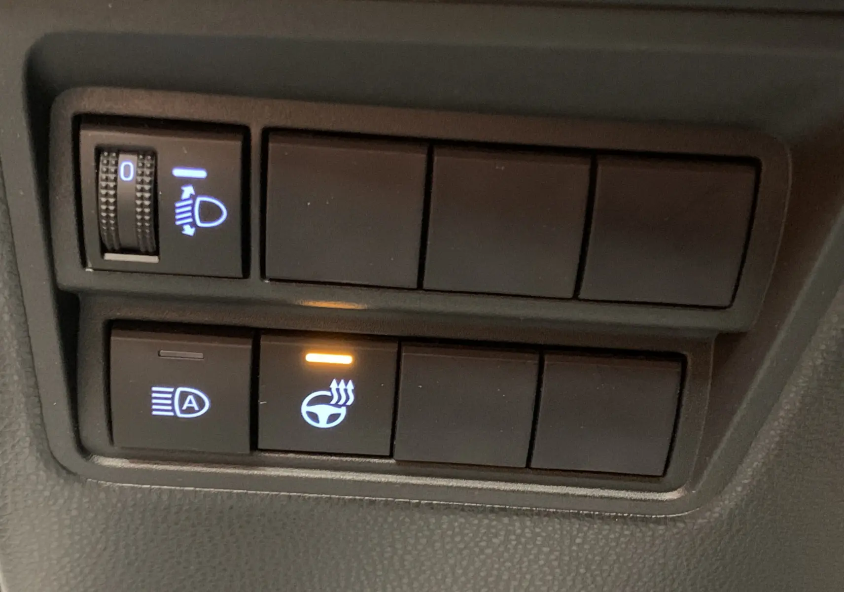 Gros plan sur les commandes de réglage des phares et du volant chauffant de la Toyota Yaris blanche.