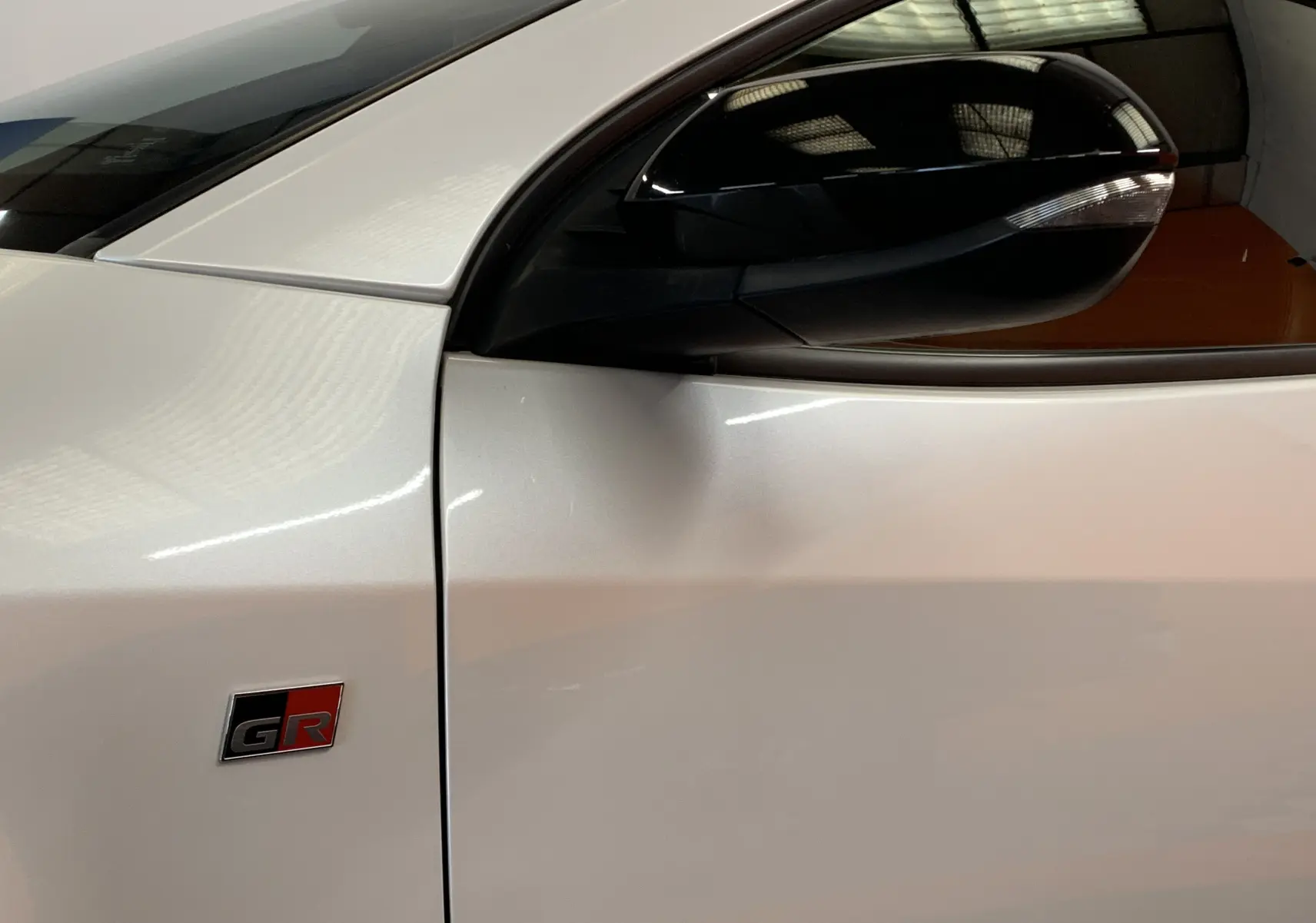 Gros plan sur la porte côté gauche blanche métal d'une Toyota Yaris GR avec logo sport et rétroviseur noir brillant.