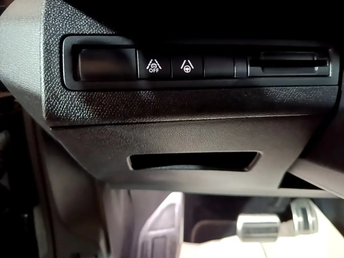 Vue rapprochée des commandes d'assistance à la conduite sous le tableau de bord noir du Peugeot 3008 GT bleu.