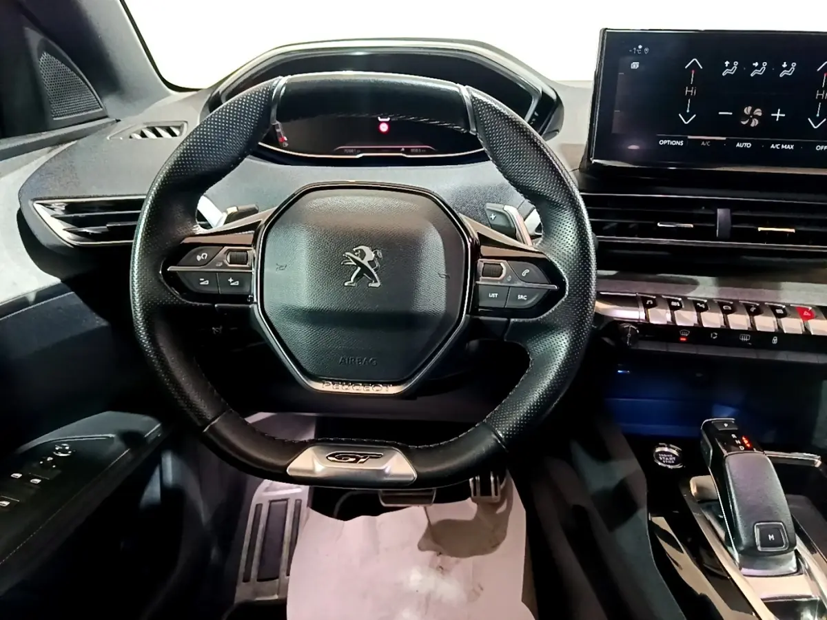 Vue intérieure centrée sur le volant cuir multifonctions noir du Peugeot 3008 GT avec tableau de bord numérique et écran tactile.