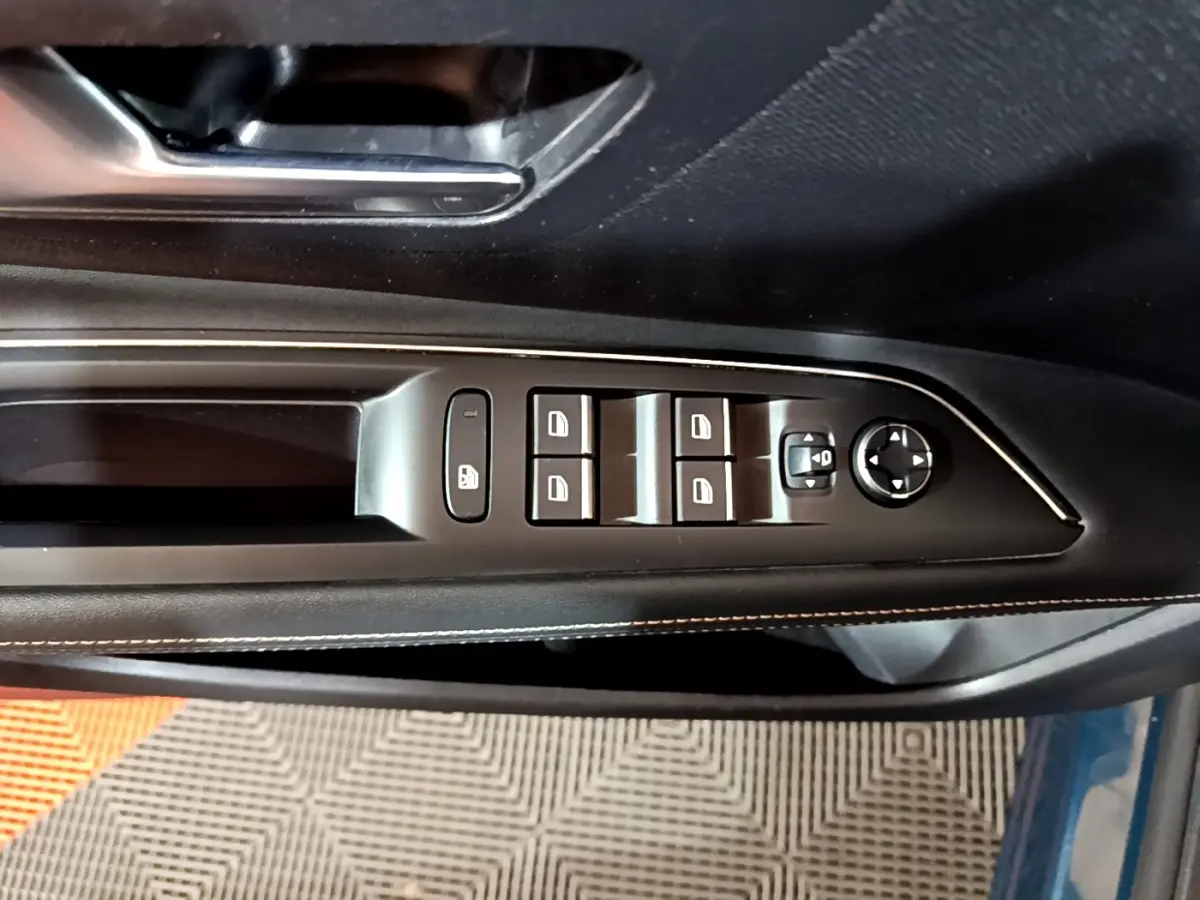 Vue rapprochée des commandes de lève-vitres et rétroviseurs sur la porte côté gauche d’un Peugeot 3008 bleu.