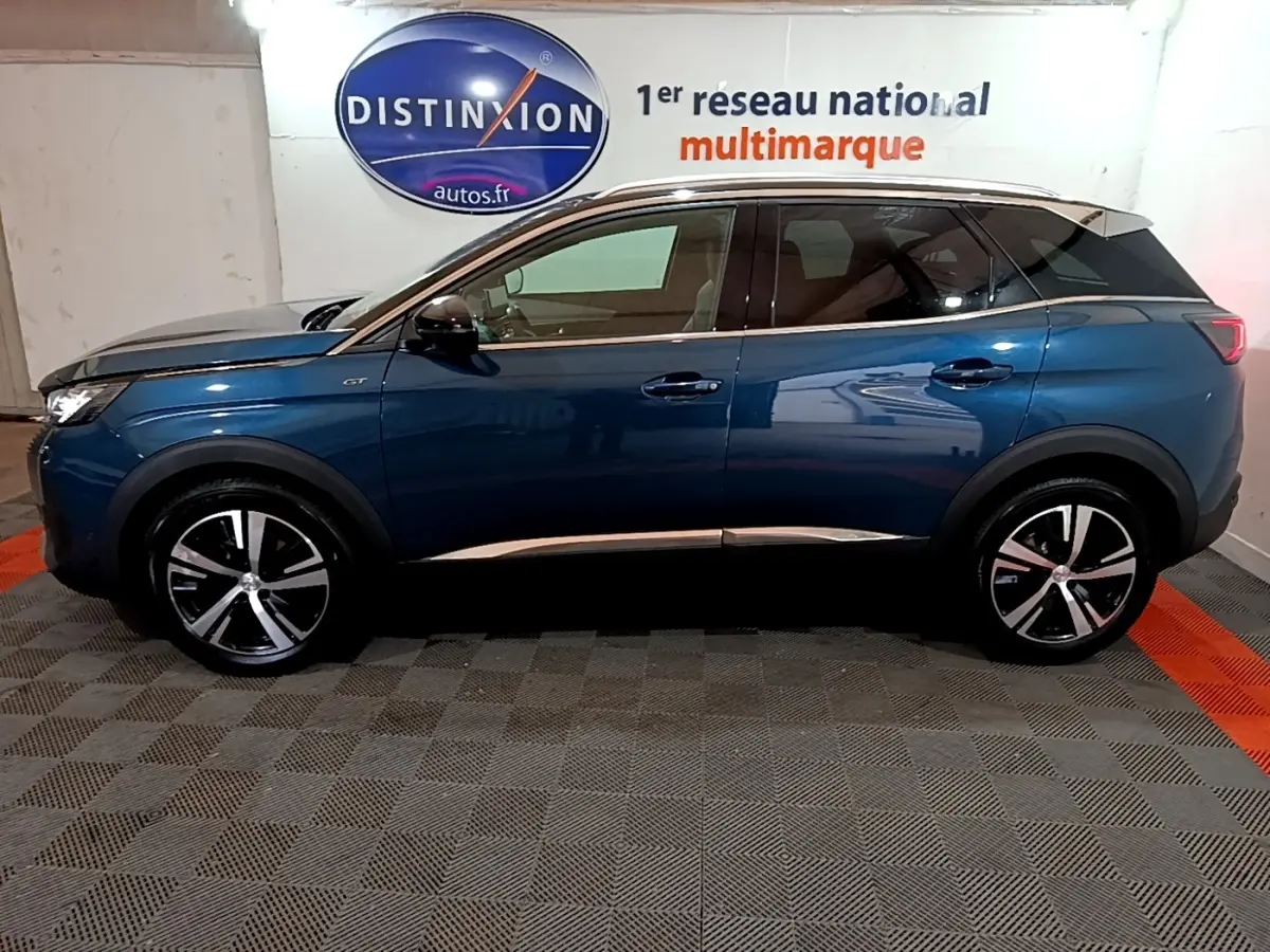 Vue latérale droite d'un Peugeot 3008 GT bleu 2021 avec jantes alliage et toit noir en intérieur showroom.