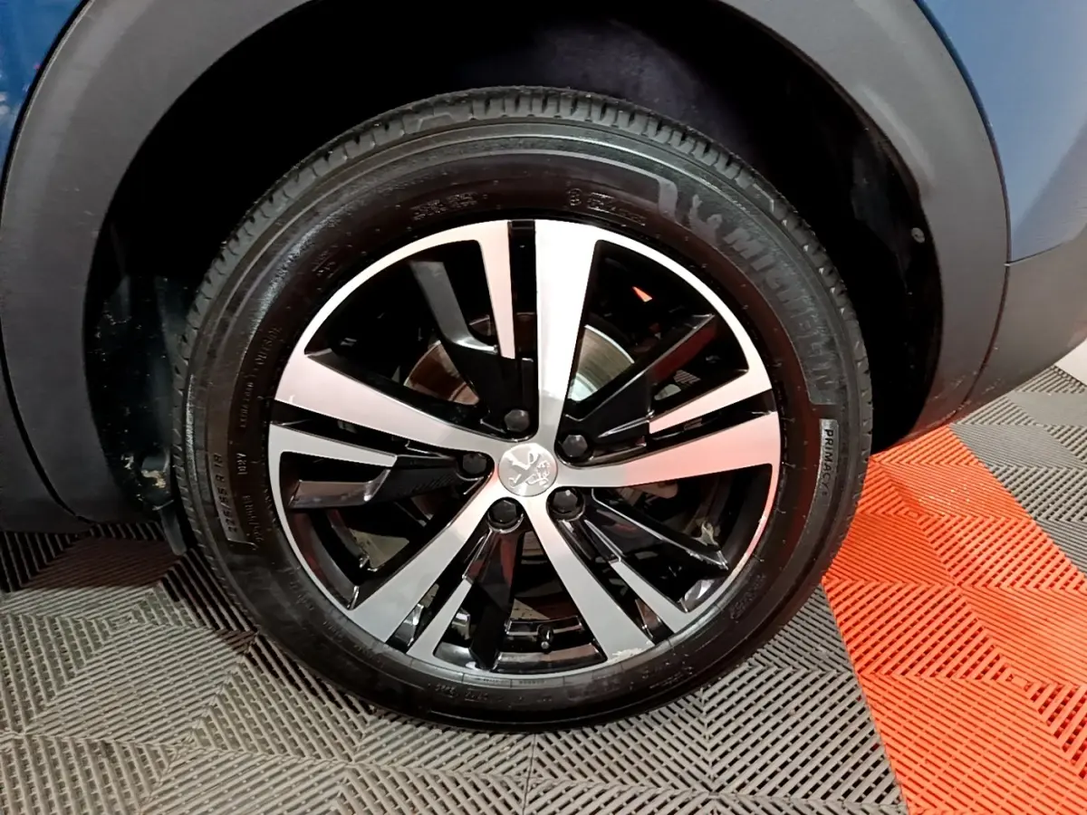 Gros plan sur la roue avant droite du Peugeot 3008 bleu, avec jante alliage bicolore noire et argentée.