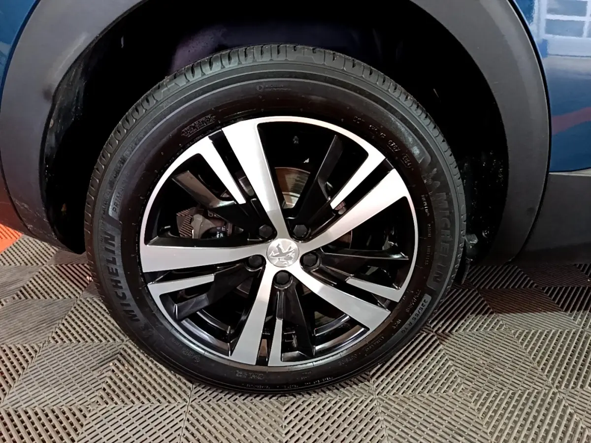 Gros plan sur la roue avant droite d’un Peugeot 3008 bleu avec jante alliage bicolore et pneu Michelin.