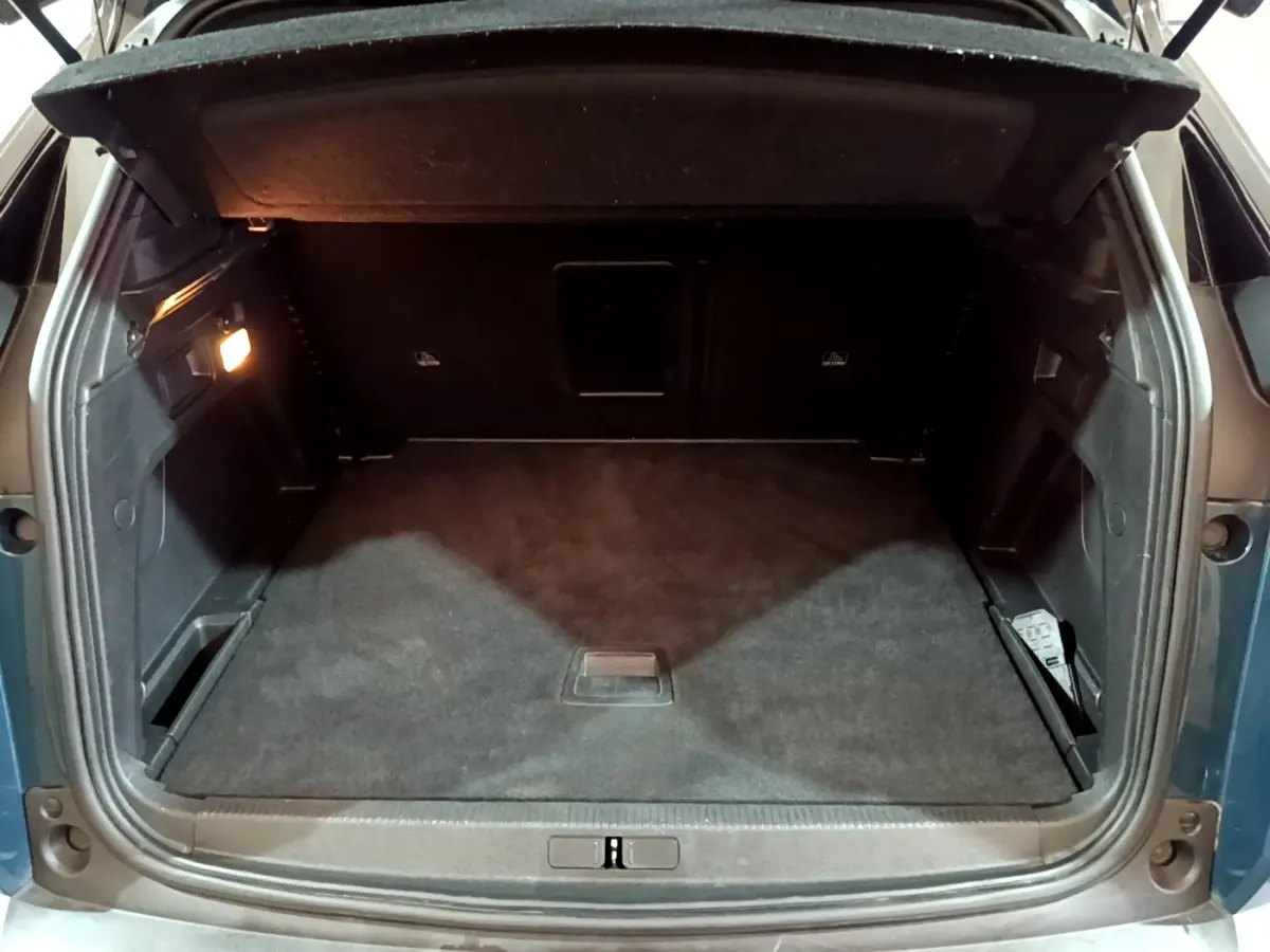 Coffre ouvert vu de l'arrière du Peugeot 3008 PureTech 130 bleu, espace de rangement spacieux et éclairé.