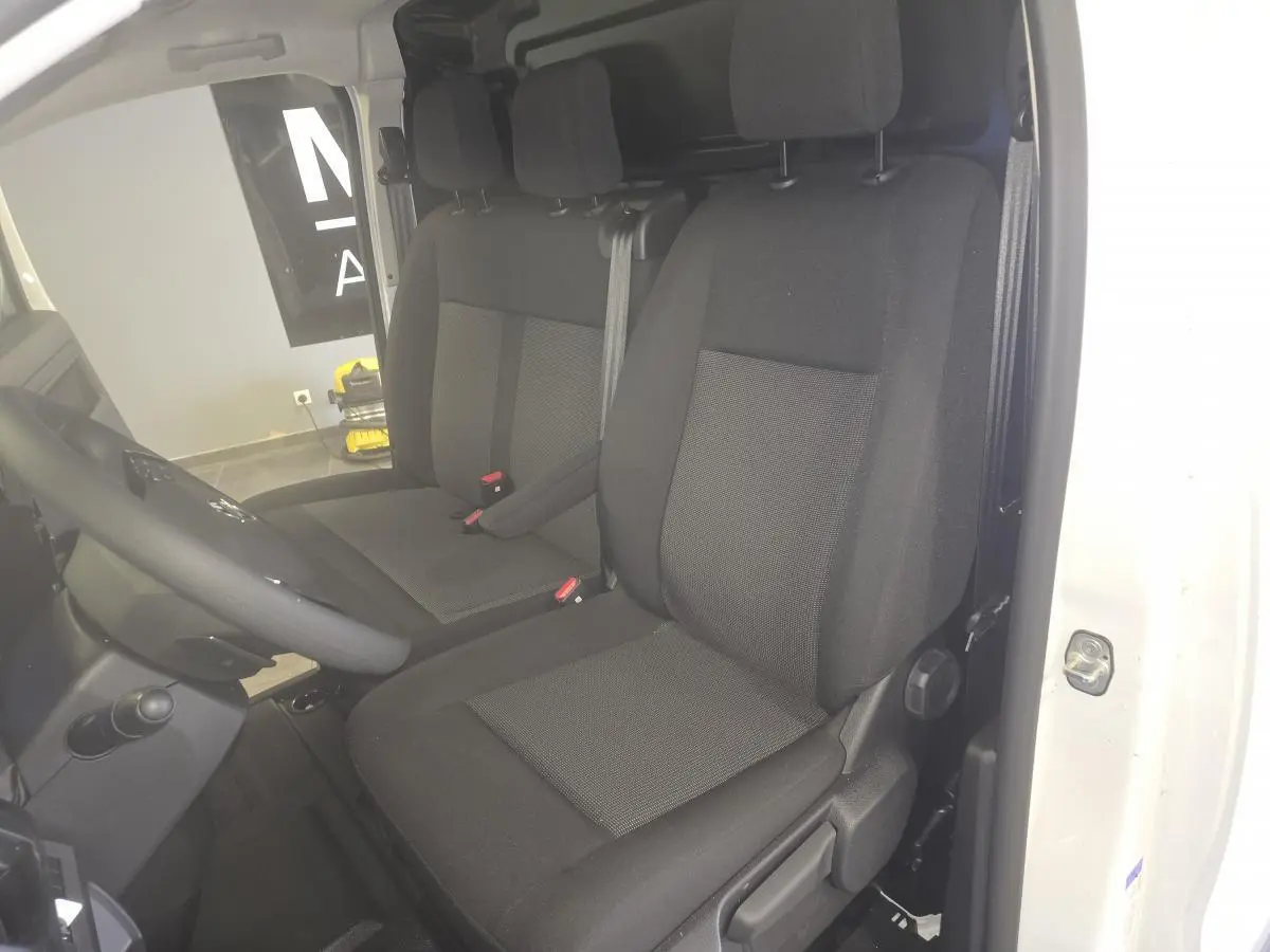 Vue intérieure côté conducteur de l'Opel Vivaro blanc 2025, montrant les sièges tissu bi-ton noir et gris.