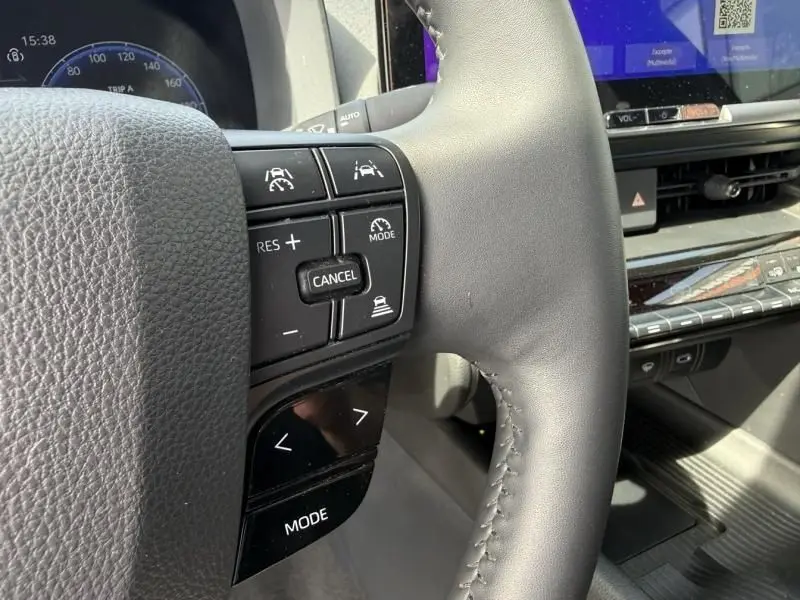 Gros plan sur le volant côté gauche du Toyota C-HR Hybride 2024, avec commandes de régulateur et tableau de bord partiellement visible.