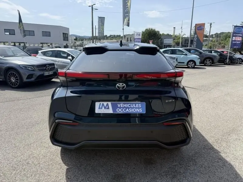 Vue arrière d’un Toyota C-HR Hybride 2024 en bleu persan, avec feux arrière continus et logo Toyota bien visibles.